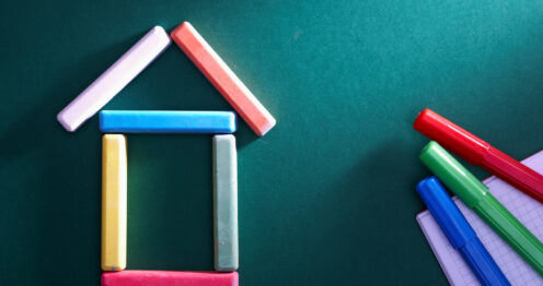 Yeşil tahta üzerinde renkli tebeşirlerden oluşturulmuş ev figürü ve renkli kalemler